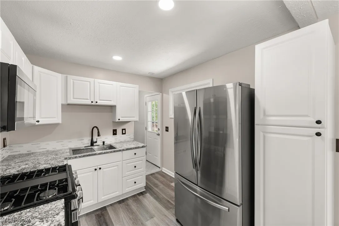 Kitchen with appliances with stainless steel finishes, white cabinetry, light wood-type flooring, light stone counters, and recessed lighting