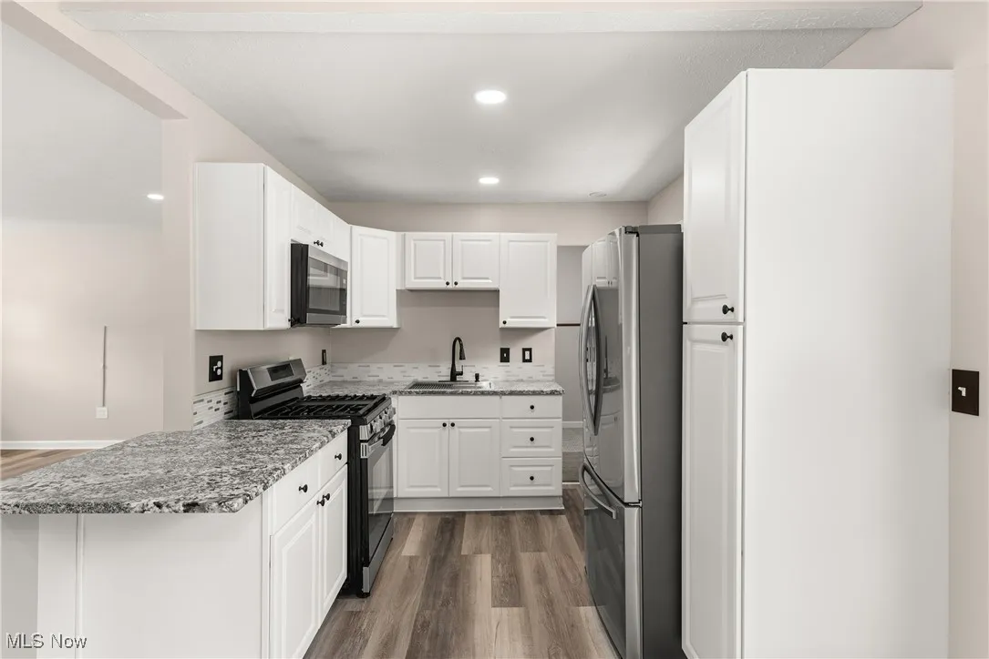Kitchen featuring appliances with stainless steel finishes, wood finished floors, white cabinetry, a peninsula, and recessed lighting