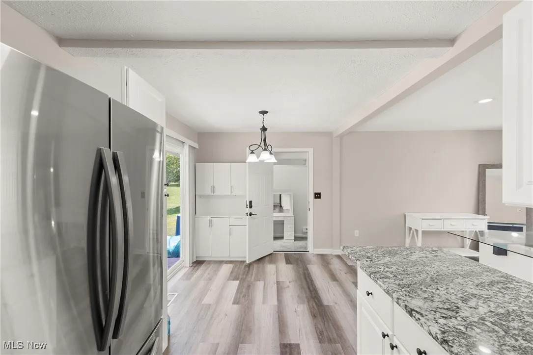 Kitchen featuring freestanding refrigerator, light wood-style floors, white cabinetry, light stone counters, and beam ceiling