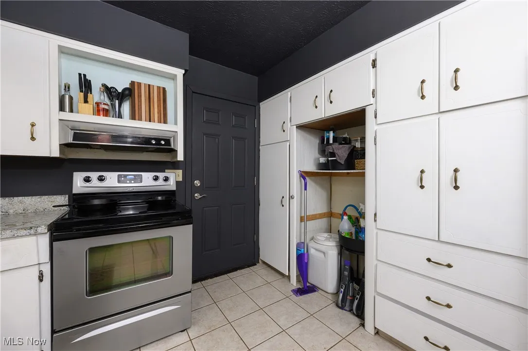 Kitchen with stainless steel electric stove, open shelves, exhaust hood, and light tile patterned floors