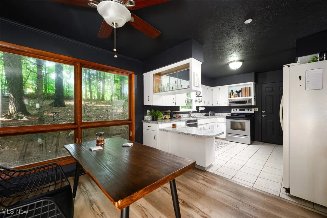 Kitchen featuring stainless steel appliances, open shelves, white cabinets, light wood-style flooring, and a ceiling fan