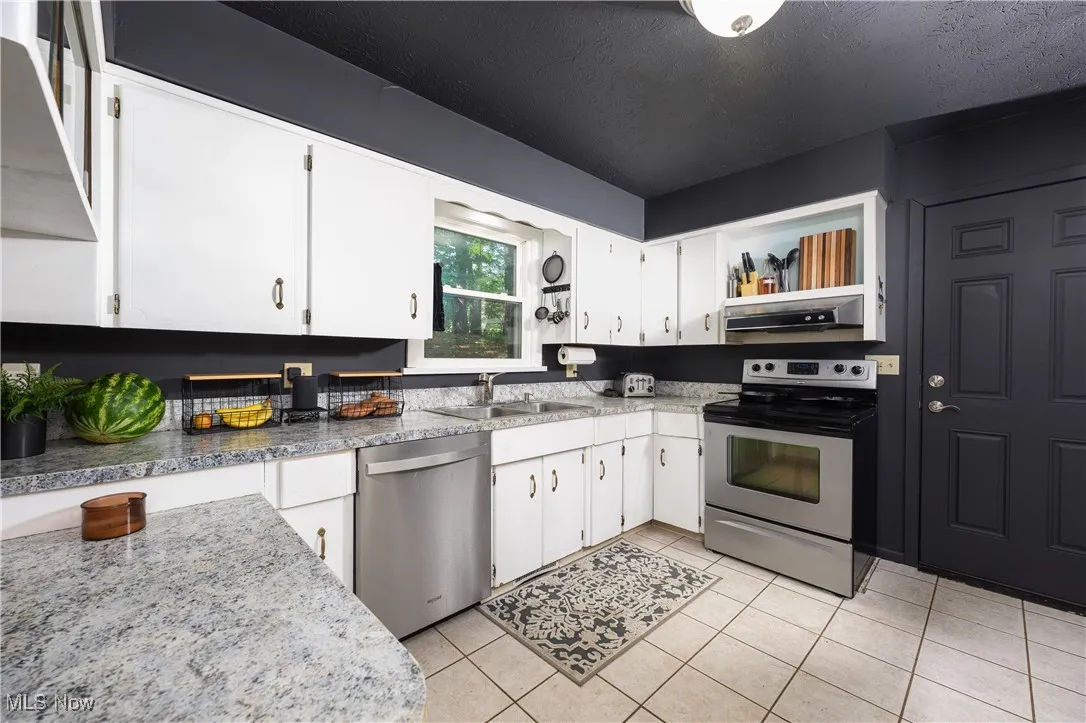 Kitchen featuring stainless steel appliances, exhaust hood, open shelves, white cabinetry, and a textured ceiling