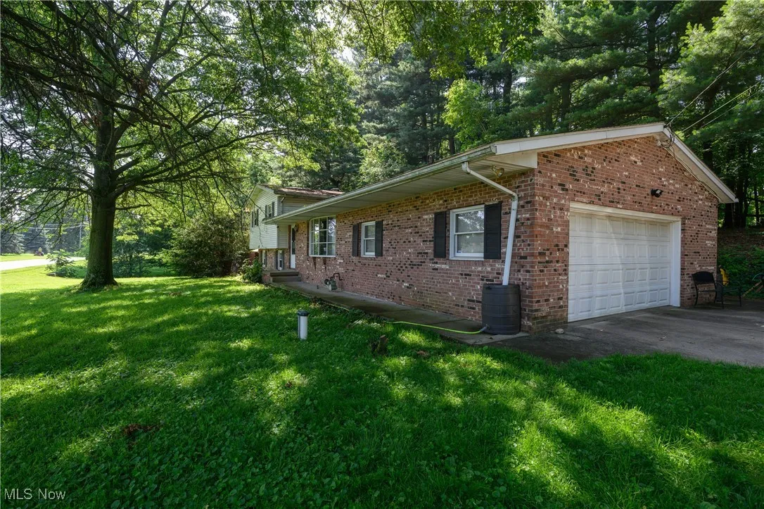 View of side of property with an attached garage, a yard, brick siding, and driveway