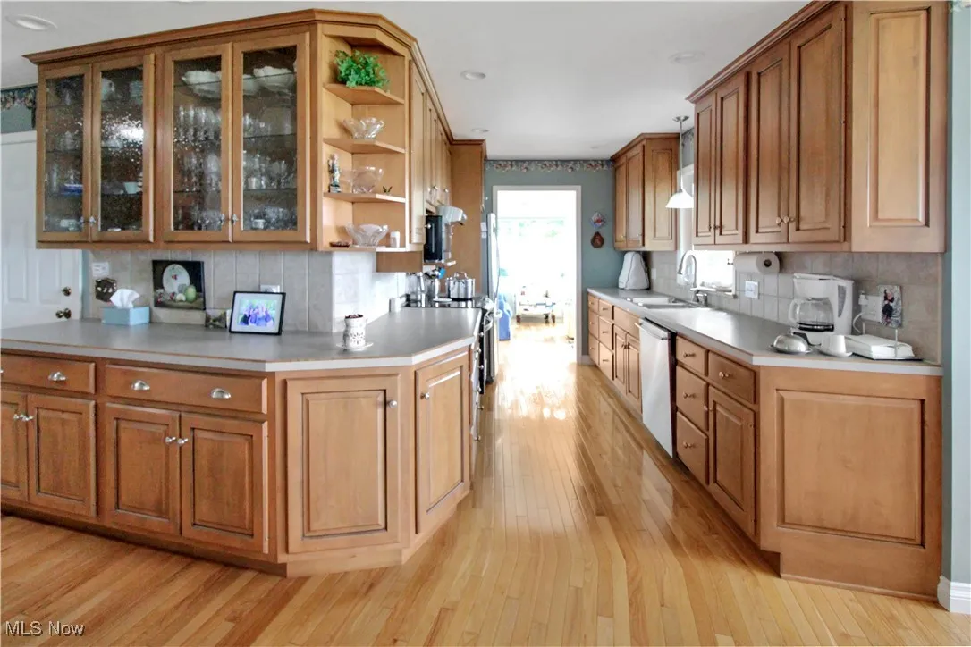 Kitchen featuring stainless steel dishwasher, light wood-style floors, open shelves, backsplash, and brown cabinets
