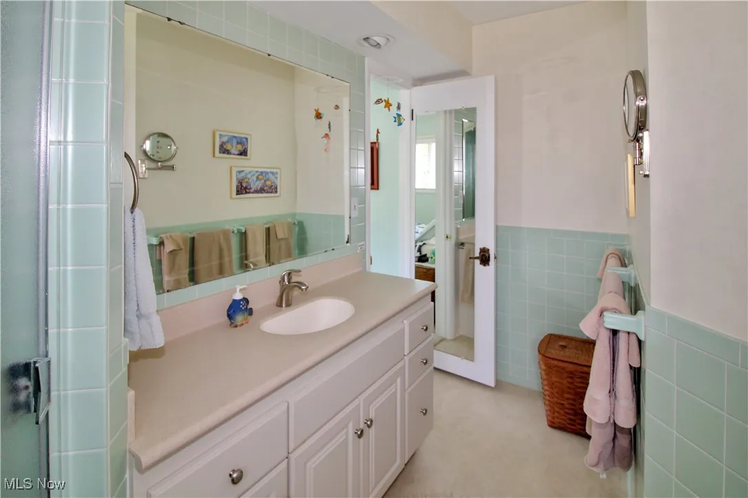 Bathroom with tile walls, vanity, wainscoting, and a shower with door