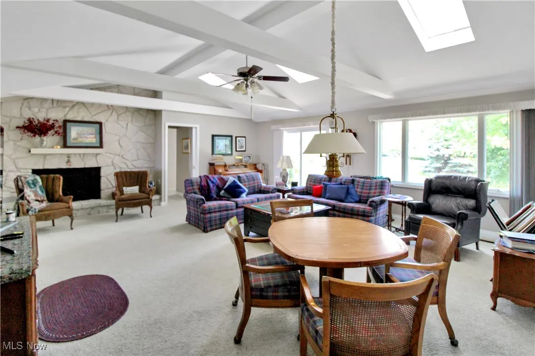 Dining space featuring a skylight, carpet, a stone fireplace, and a ceiling fan