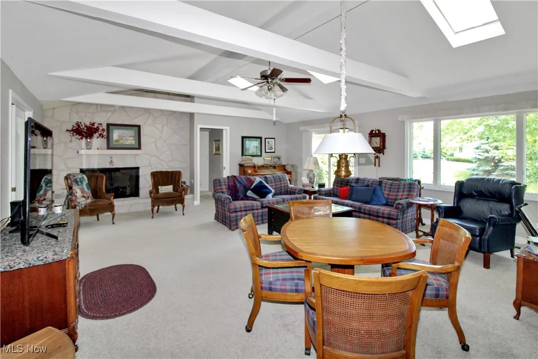 Dining space featuring a fireplace, light colored carpet, a skylight, and a ceiling fan