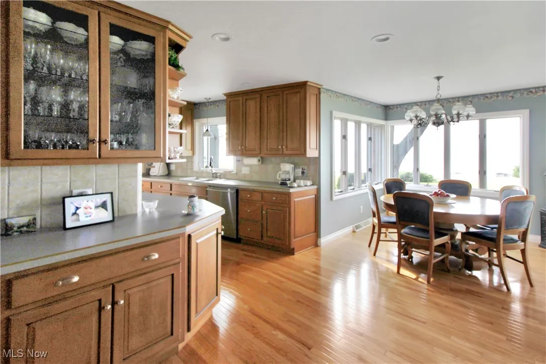 Kitchen with open shelves, a chandelier, stainless steel dishwasher, brown cabinetry, and recessed lighting