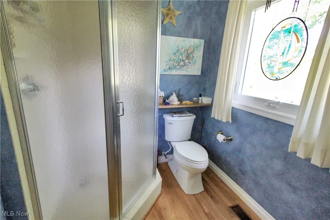 Bathroom featuring wood finished floors, a shower stall, and wallpapered walls