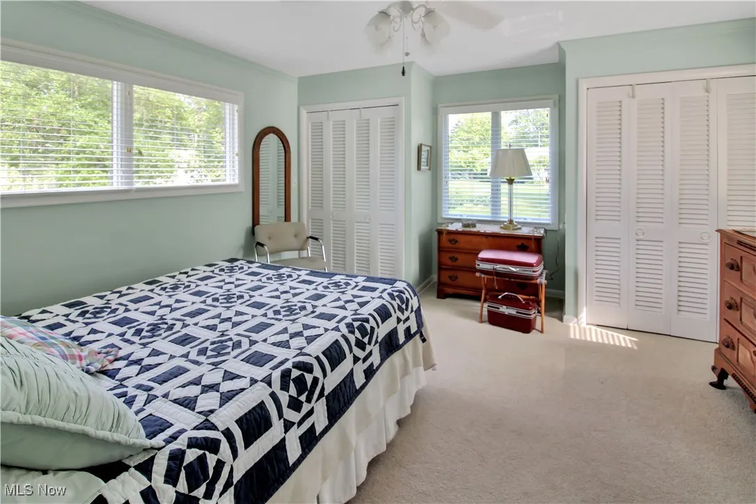 Bedroom with multiple closets, multiple windows, light colored carpet, and a ceiling fan