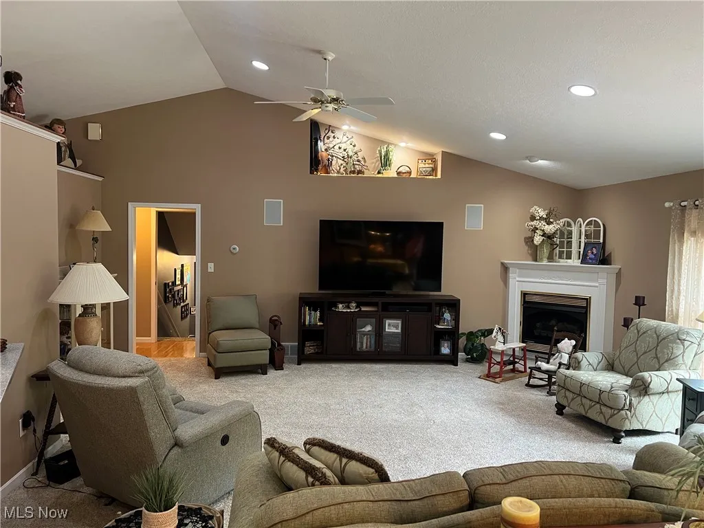 Living area featuring carpet flooring, lofted ceiling, a ceiling fan, a fireplace, and recessed lighting