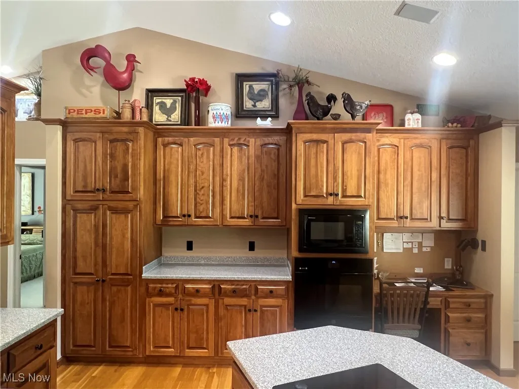 Kitchen featuring black appliances, vaulted ceiling, light countertops, light wood finished floors, and brown cabinets
