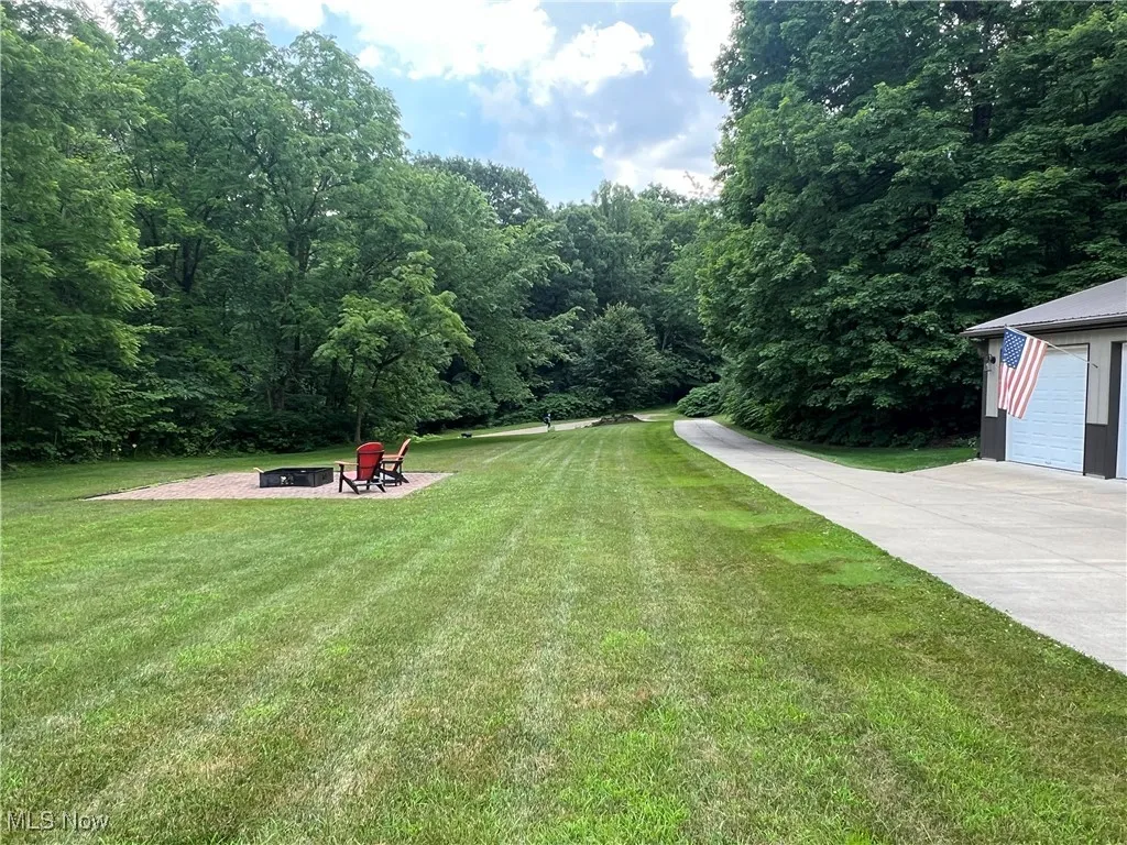 View of green lawn with a fire pit and a forest view