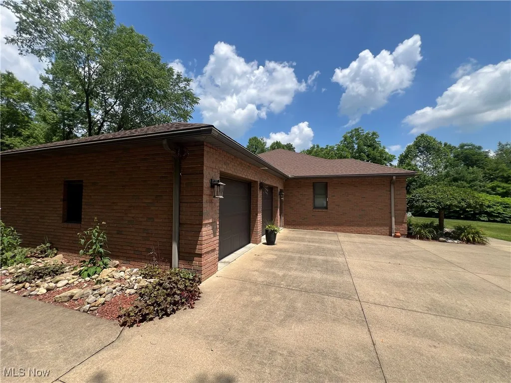 View of property exterior featuring an attached garage, concrete driveway, and brick siding