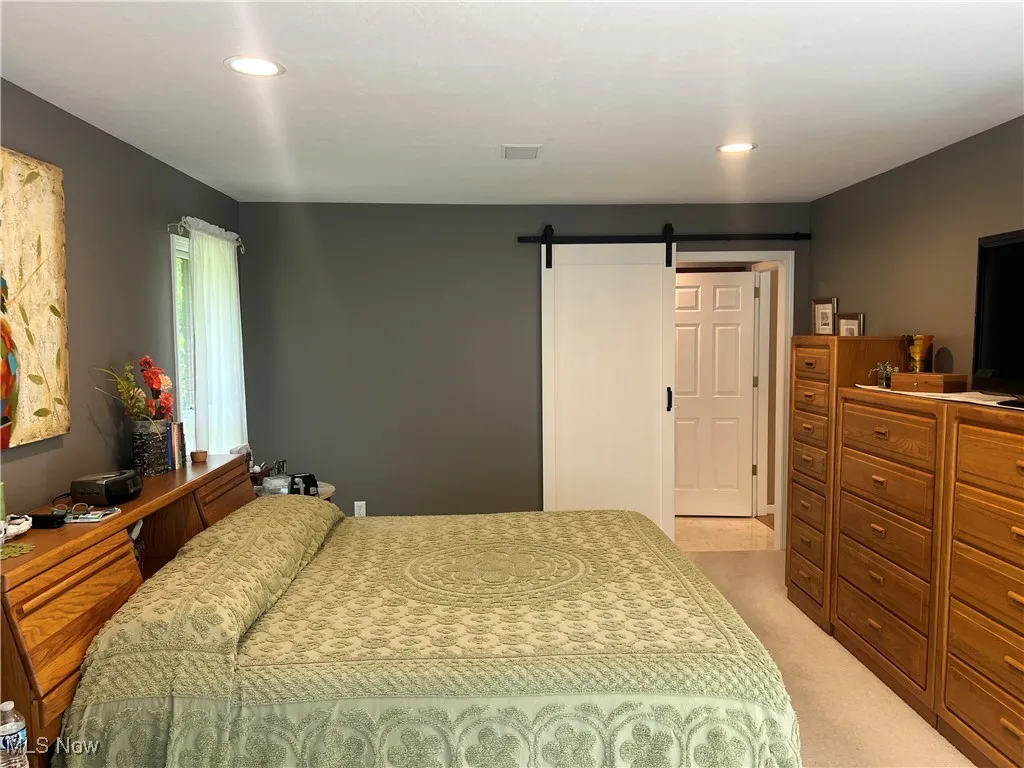 Bedroom with light carpet, a barn door, and recessed lighting