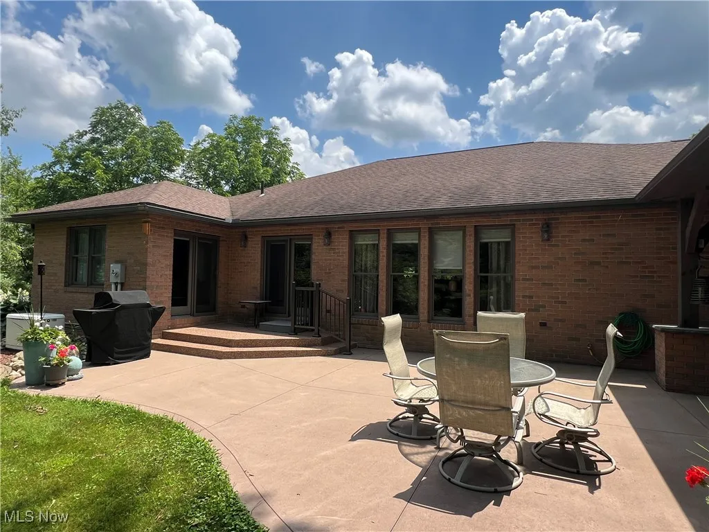 Back of house featuring brick siding, a patio, and a shingled roof