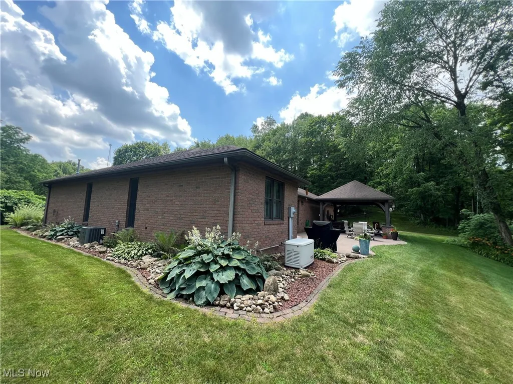 View of property exterior featuring a gazebo, brick siding, a patio area, and a lawn