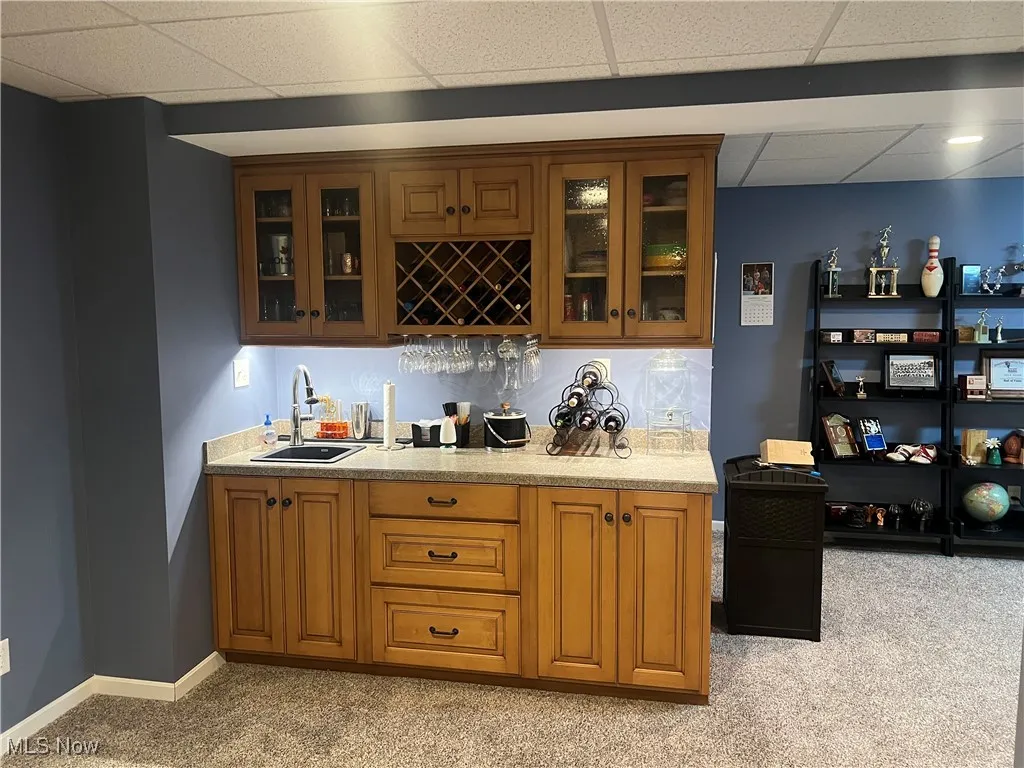 Indoor wet bar with light colored carpet and a paneled ceiling