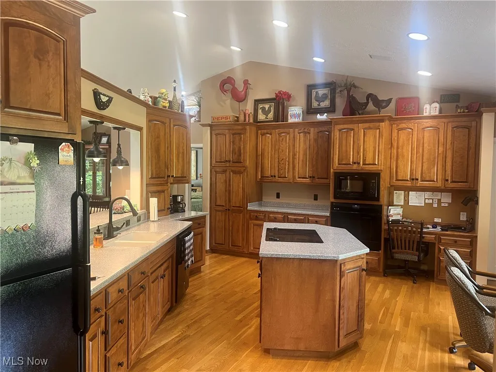 Kitchen with black appliances, a kitchen island, light wood-style flooring, brown cabinetry, and built in desk