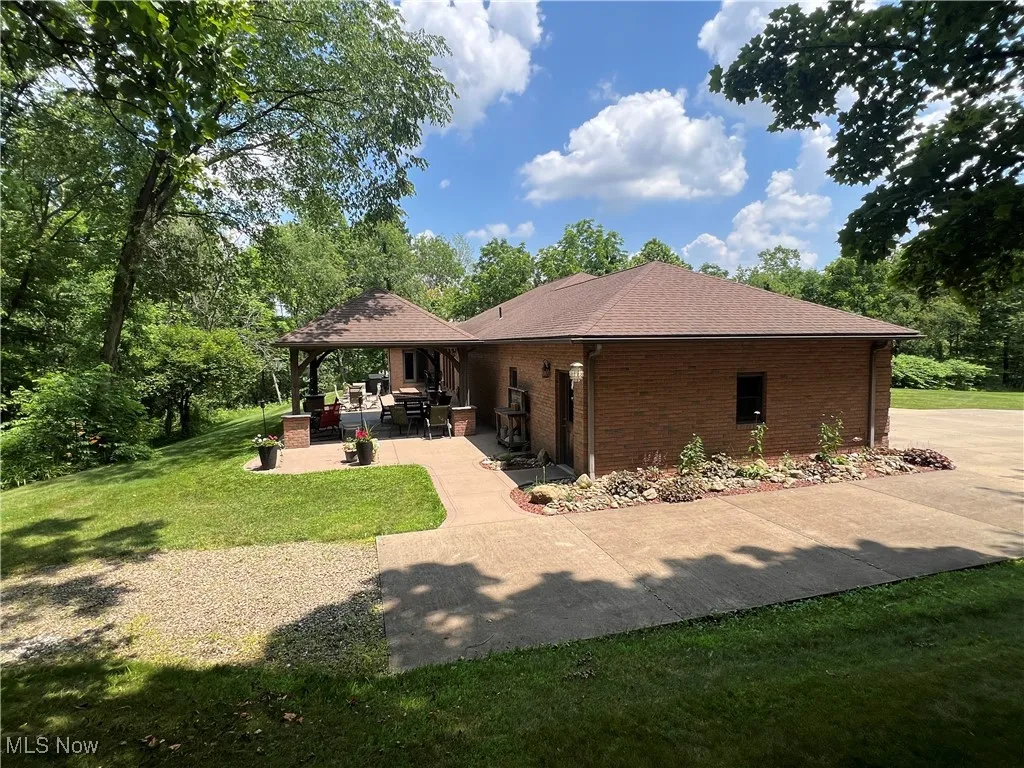 Back of house with brick siding, a lawn, a patio area, and a shingled roof