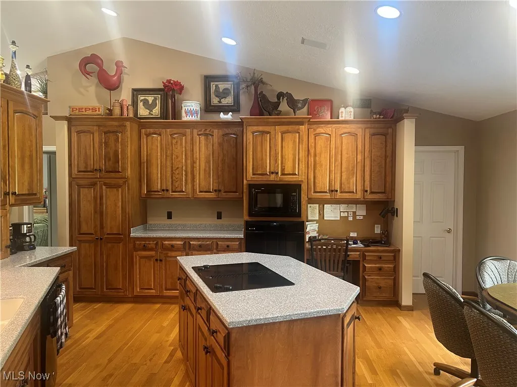 Kitchen featuring black appliances, lofted ceiling, light wood-style floors, brown cabinets, and a center island