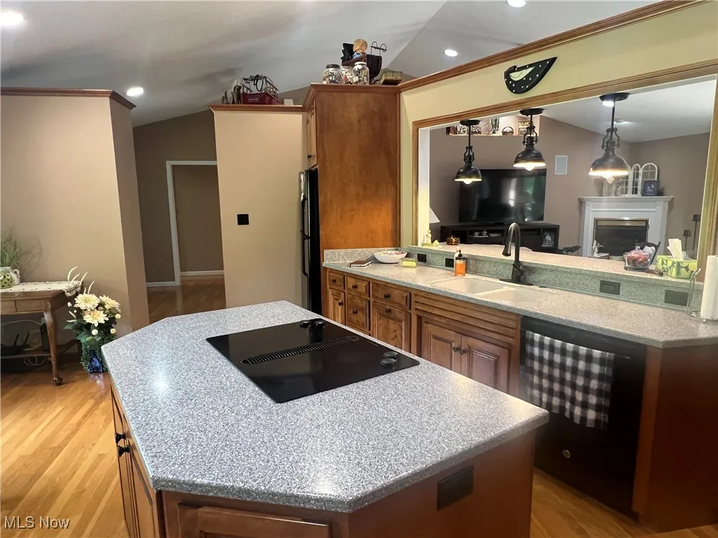 Kitchen featuring black appliances, brown cabinetry, a center island, light wood-style flooring, and decorative light fixtures