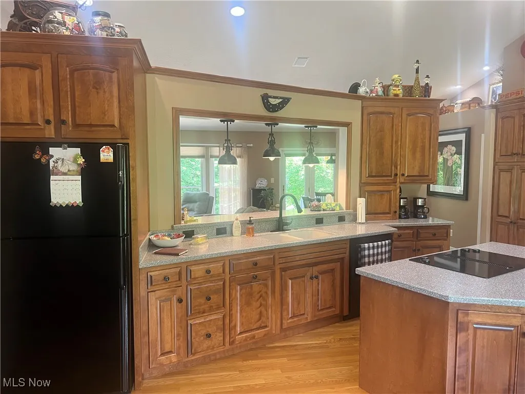 Kitchen with black appliances, brown cabinetry, light wood-style floors, hanging light fixtures, and ornamental molding