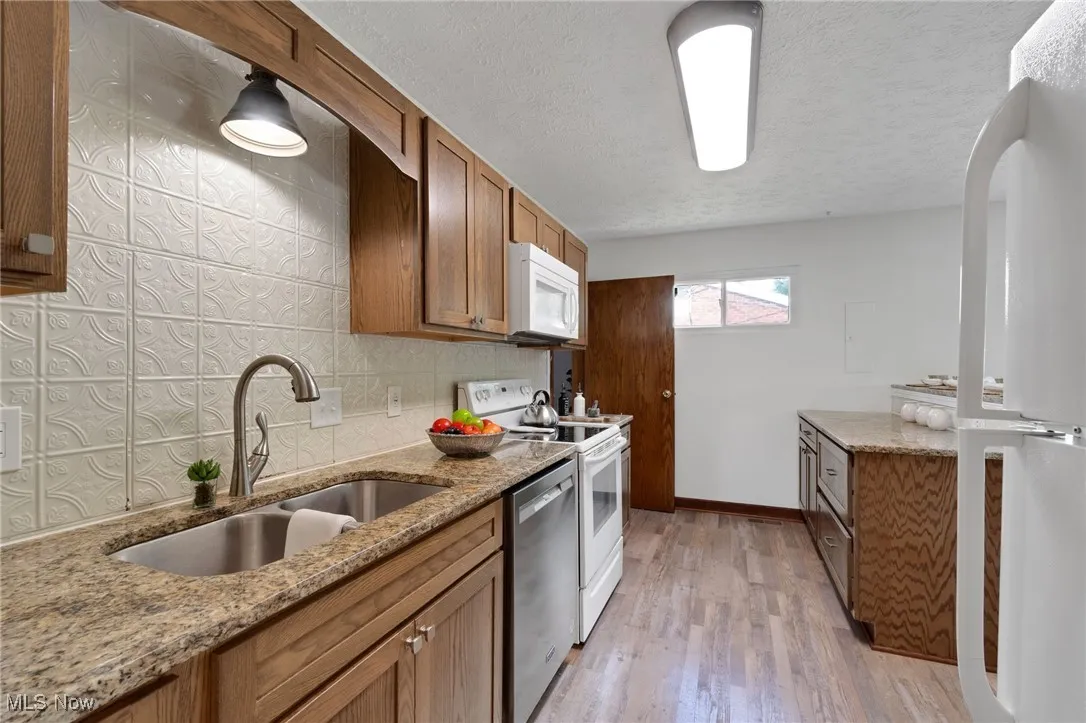 Kitchen featuring white appliances, brown cabinets, light wood-style floors, light stone counters, and backsplash