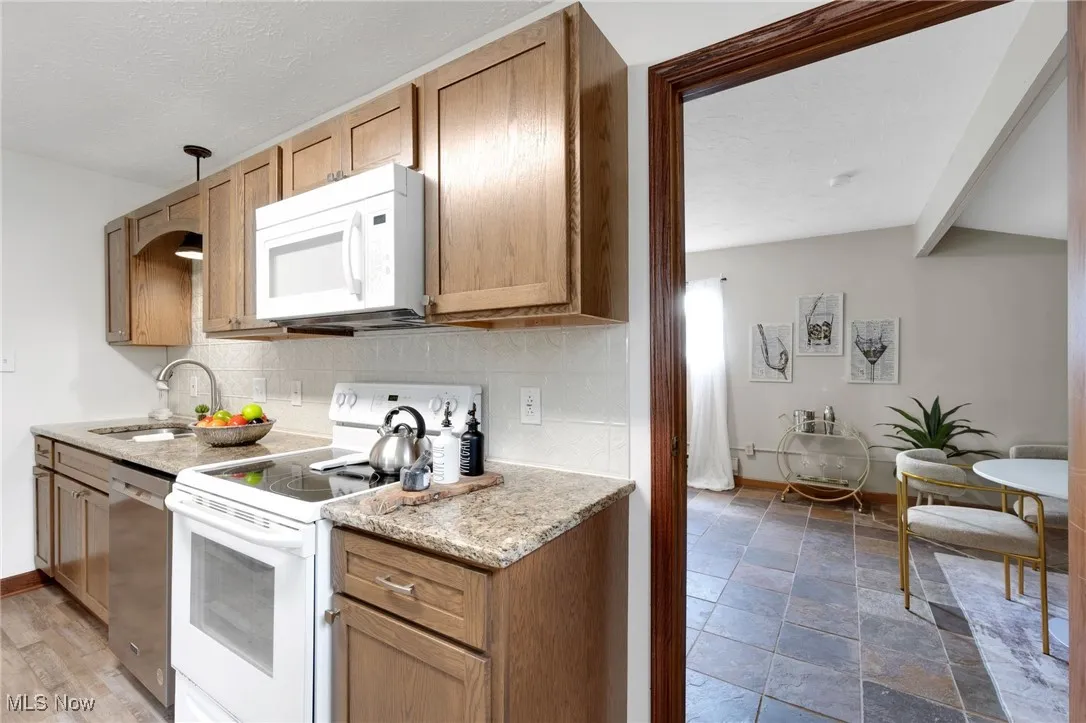 Kitchen with white appliances, tasteful backsplash, light stone finish floors, a textured ceiling, and beam ceiling