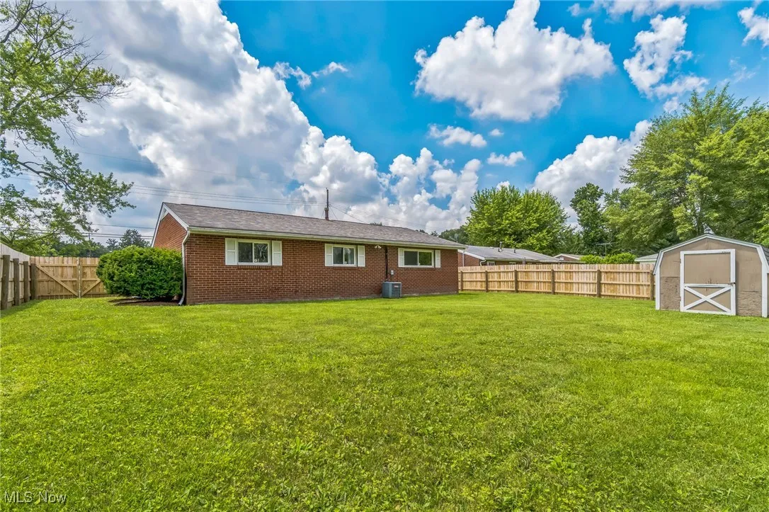 Rear view of property with a fenced backyard, brick siding, and a storage shed