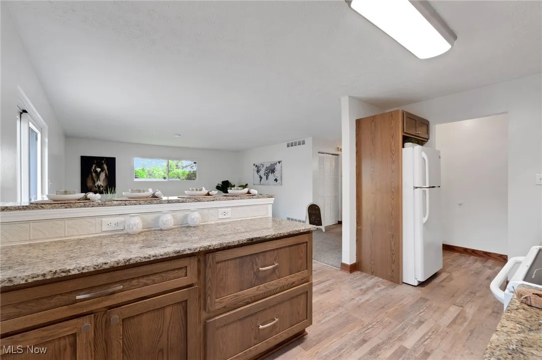 Kitchen with freestanding refrigerator, light wood-style flooring, brown cabinets, range, and light stone counters