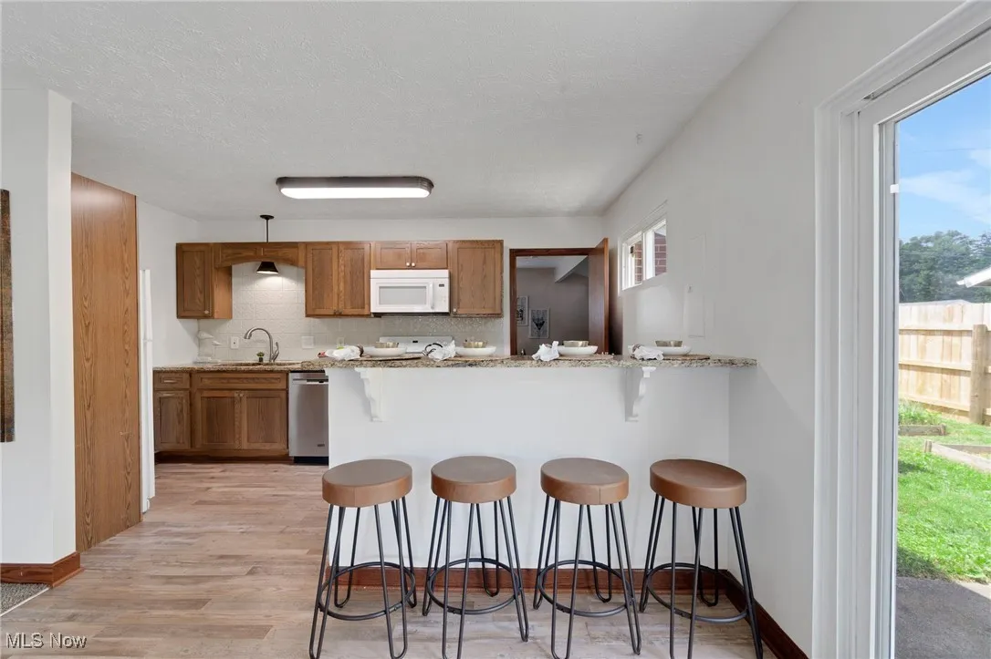 Kitchen with white microwave, a breakfast bar area, a peninsula, light wood-type flooring, and brown cabinetry