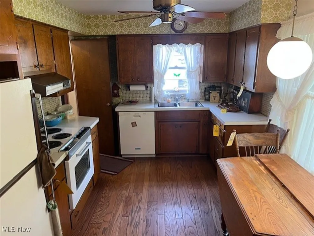 Kitchen featuring white appliances, dark wood-style flooring, wall chimney range hood, light countertops, and wallpapered walls