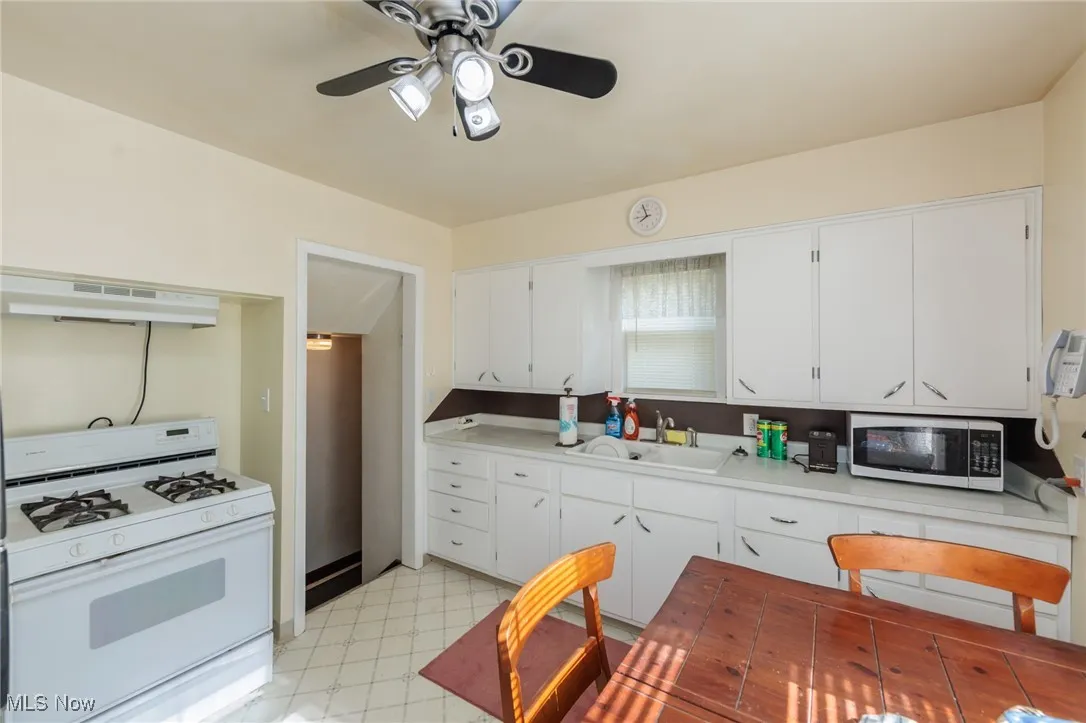 Kitchen with white range with gas cooktop, ventilation hood, light floors, ceiling fan, and light countertops