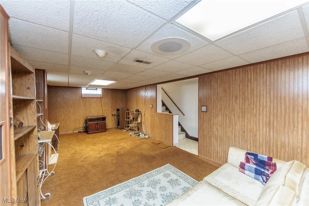 Living area featuring carpet, wooden walls, stairway, and a paneled ceiling