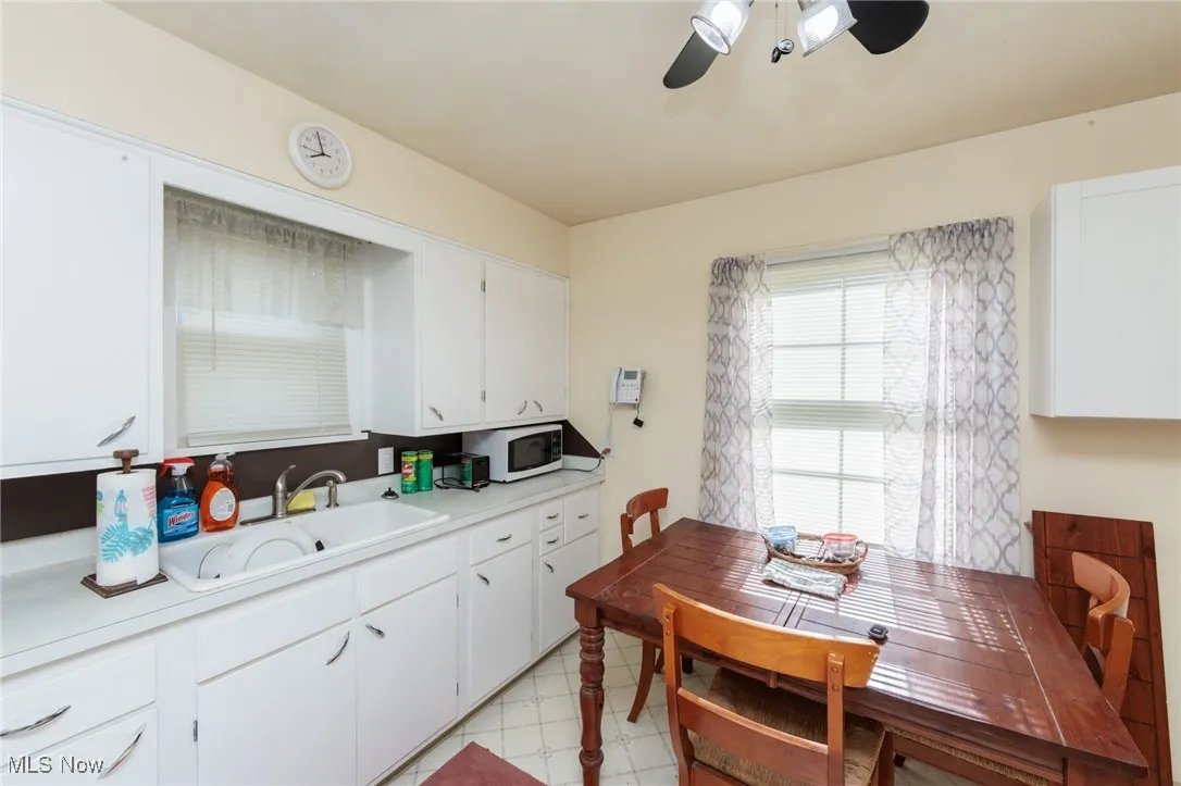 Kitchen with white microwave, light countertops, a ceiling fan, white cabinets, and light flooring