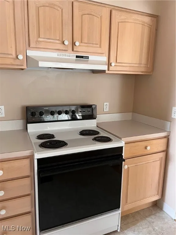 Kitchen featuring range, wall chimney exhaust hood, light brown cabinetry, and light countertops