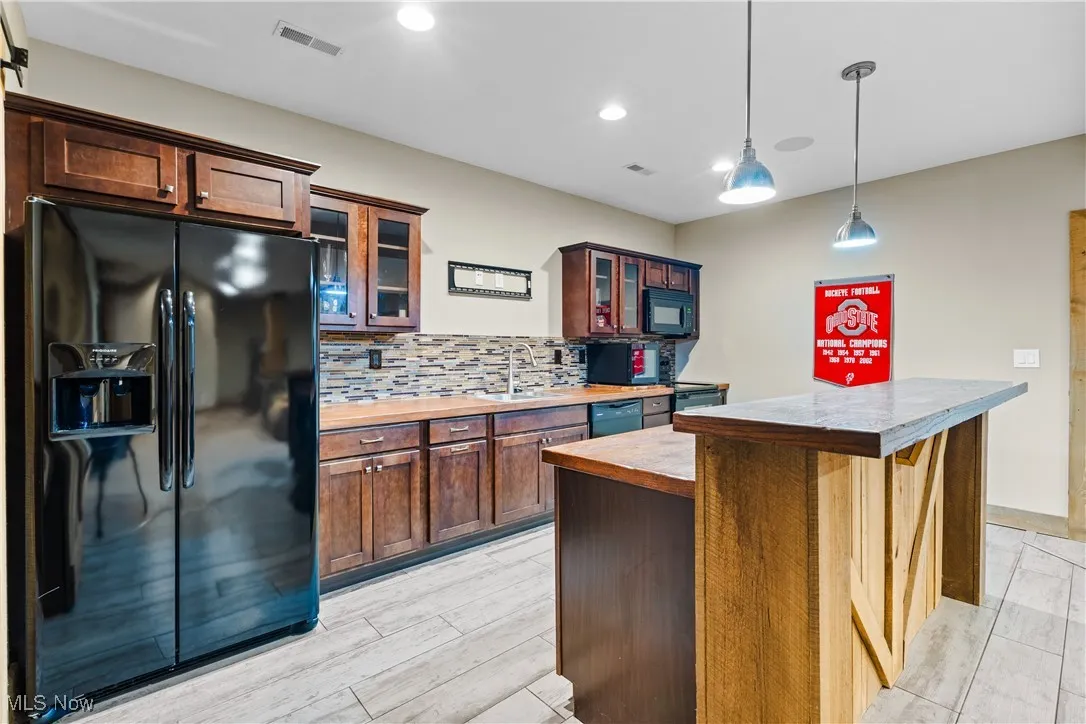 Kitchen with black appliances, backsplash, glass insert cabinets, pendant lighting, and light countertops