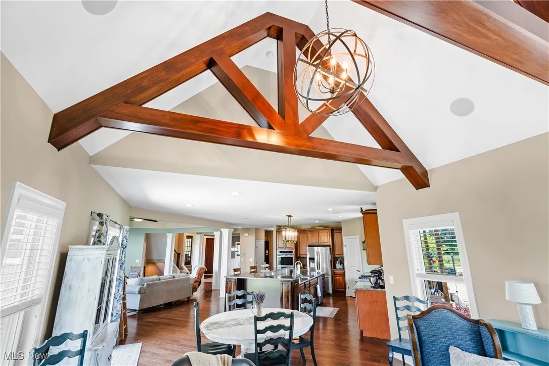 Dining area with a chandelier, high vaulted ceiling, beamed ceiling, and dark wood-style flooring