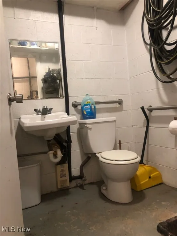 Half bath featuring unfinished concrete floors and concrete block wall