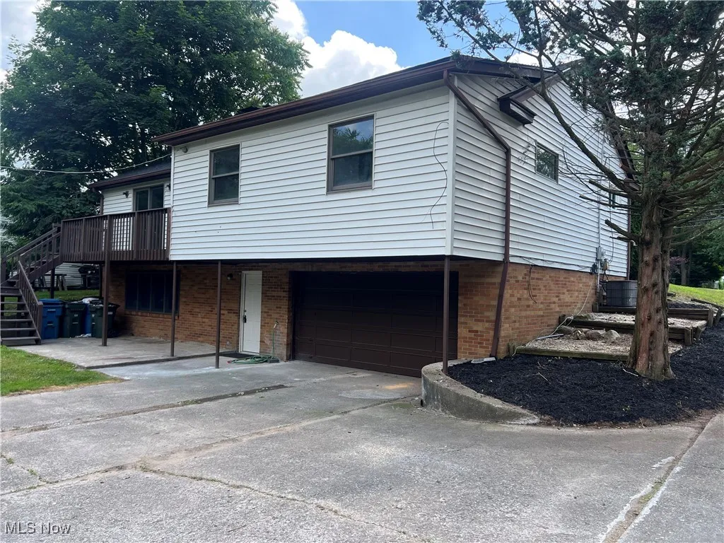 View of front of property with brick siding, stairs, driveway, a garage, and a deck