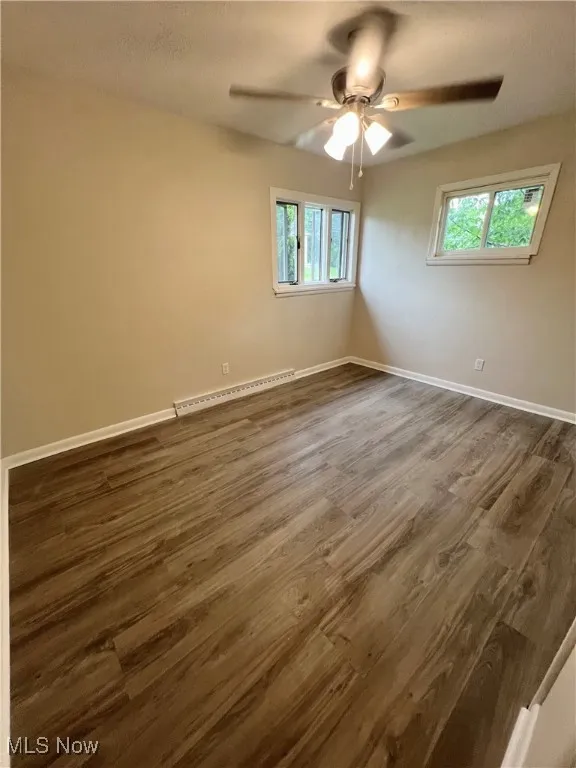 Empty room with baseboard heating, dark wood finished floors, and a ceiling fan