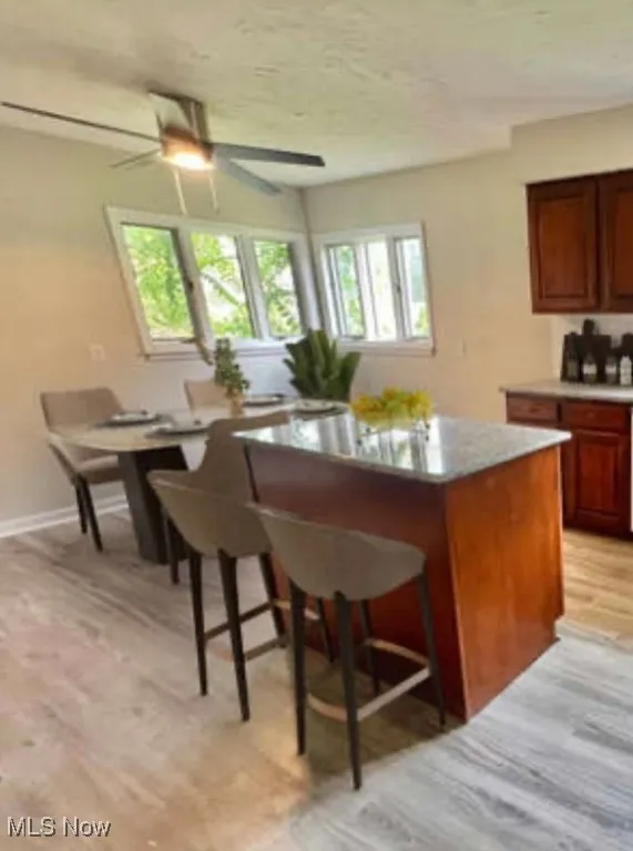 Kitchen featuring a kitchen breakfast bar, a kitchen island, light wood-type flooring, a ceiling fan, and brown cabinets