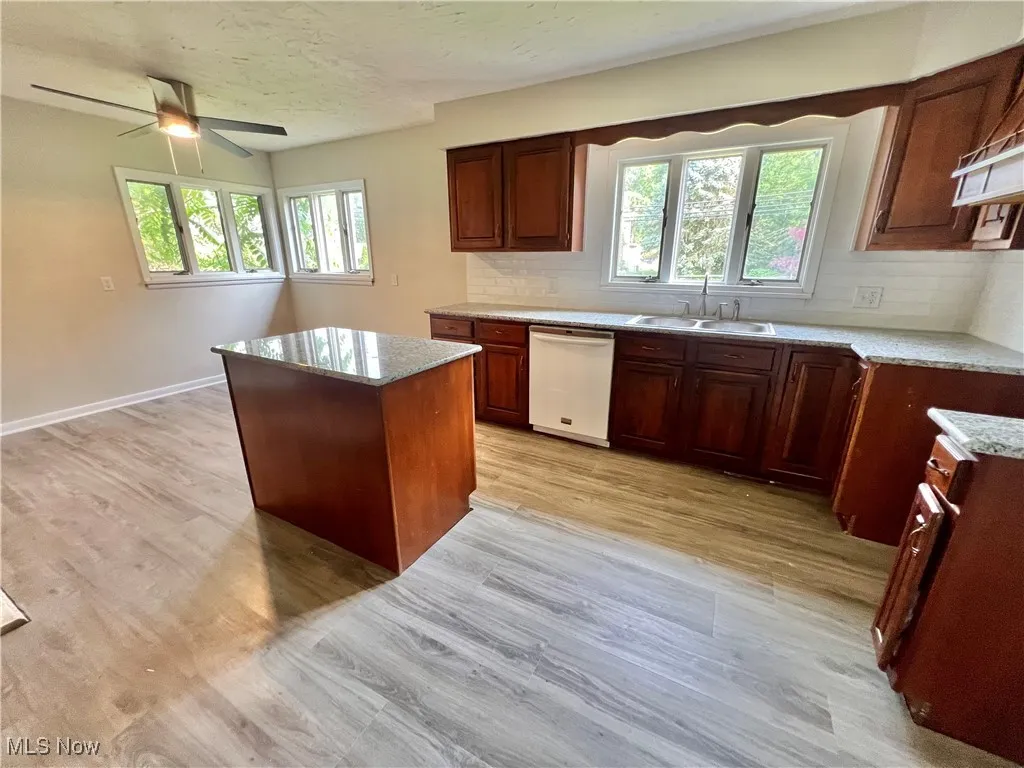 Kitchen featuring dishwasher, tasteful backsplash, a ceiling fan, a kitchen island, and light wood-style floors