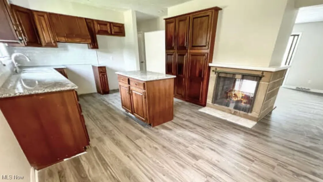 Kitchen with light wood-style flooring, a multi sided fireplace, a center island, and light stone counters