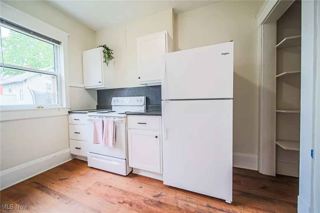 Kitchen with white appliances, dark countertops, light wood-style flooring, white cabinetry, and baseboards