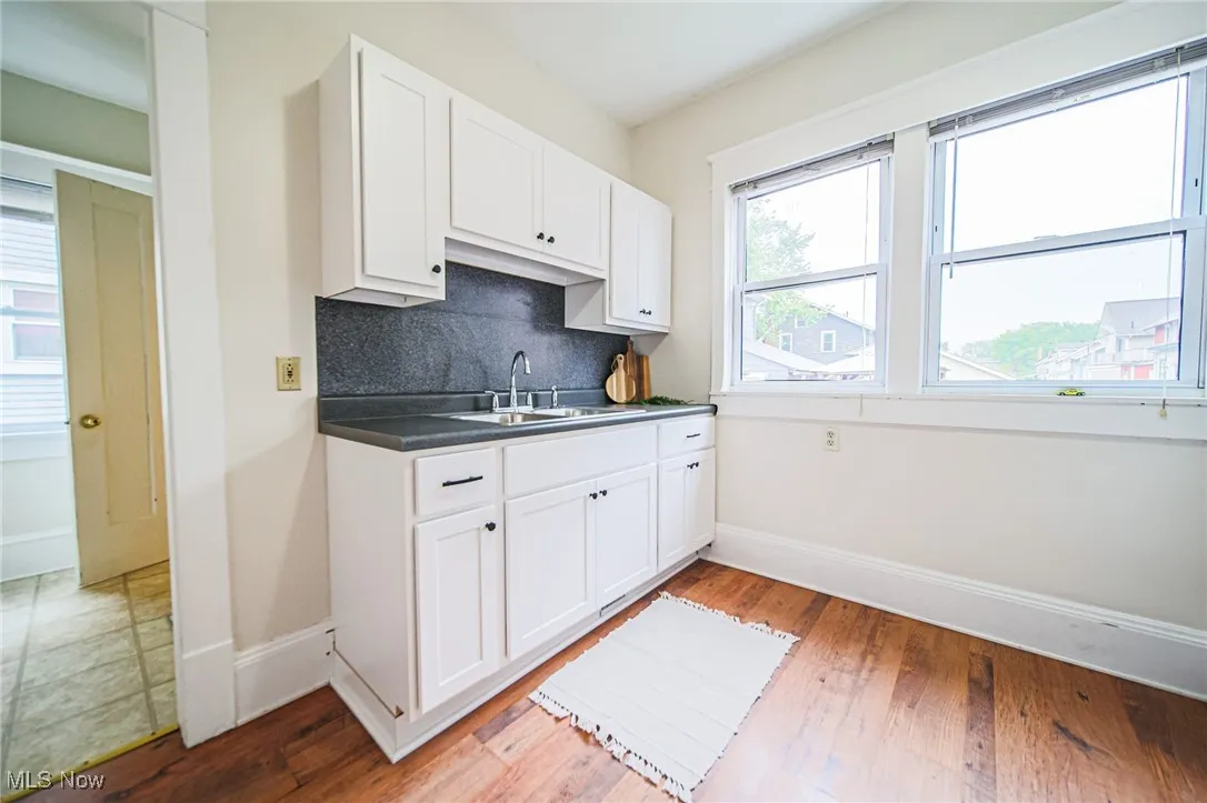 Kitchen featuring a sink, baseboards, white cabinets, and light wood-style floors