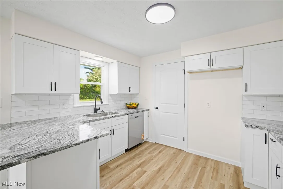 Kitchen featuring dishwasher, light stone counters, and white cabinets