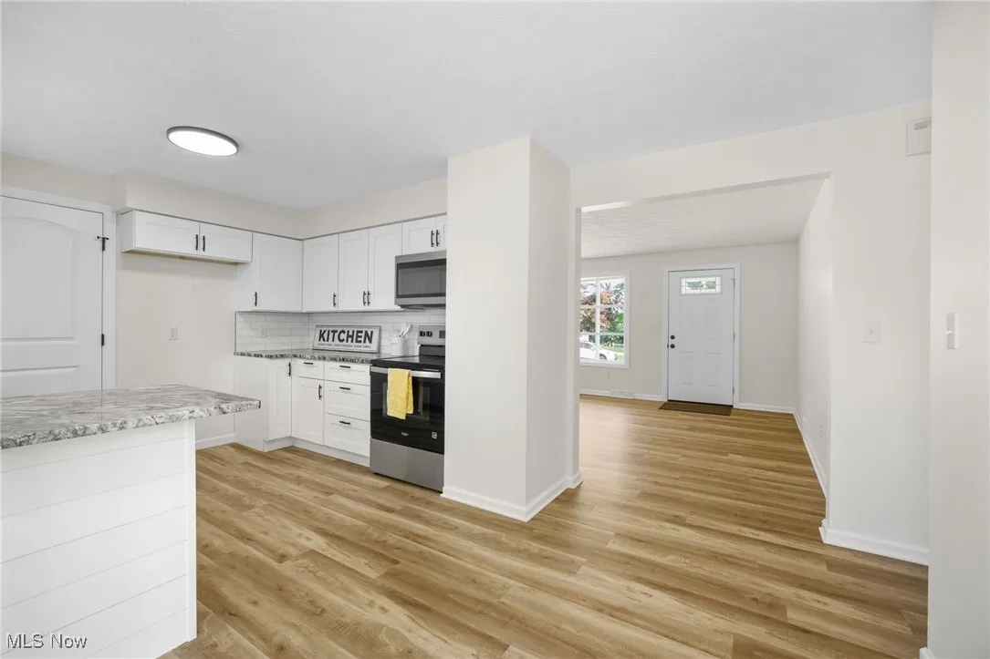 Kitchen featuring appliances with stainless steel finishes, light wood finished floors, white cabinetry, backsplash, and light stone countertops