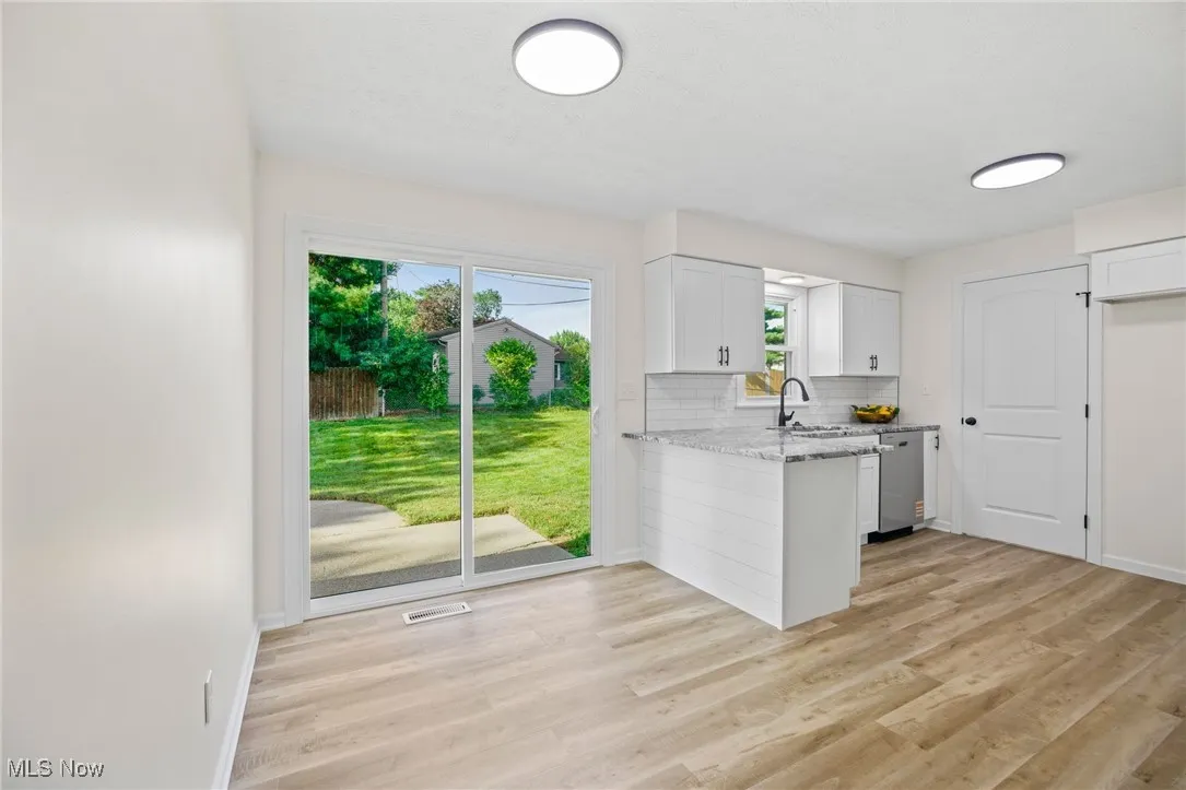 Kitchen featuring white cabinets, a peninsula, light wood-type flooring, and backsplash